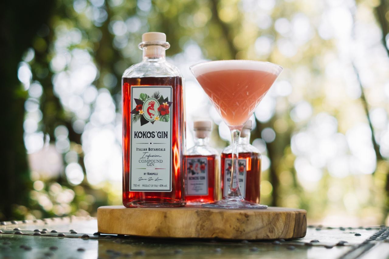 Bottiglia di Kokos' Gin accanto a un cocktail rosa su un tagliere di legno